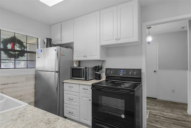 kitchen featuring pendant lighting, white cabinets, wooden walls, hardwood / wood-style flooring, and stainless steel appliances