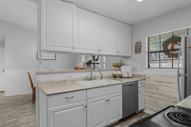 kitchen with white cabinets, stainless steel appliances, wooden walls, and sink