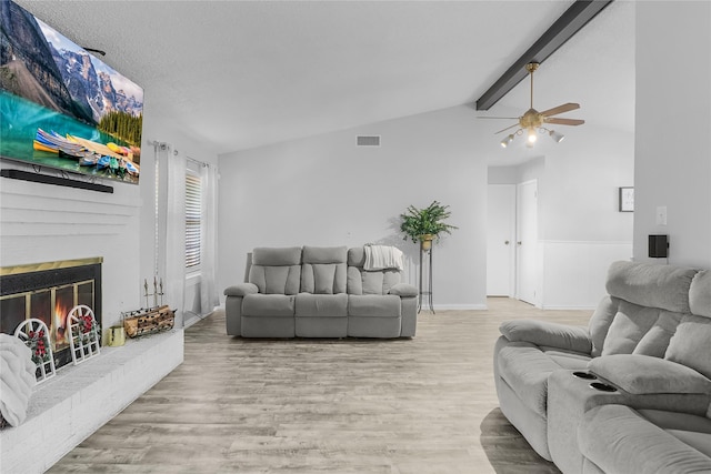 living room featuring light wood-type flooring, lofted ceiling with beams, a brick fireplace, and ceiling fan