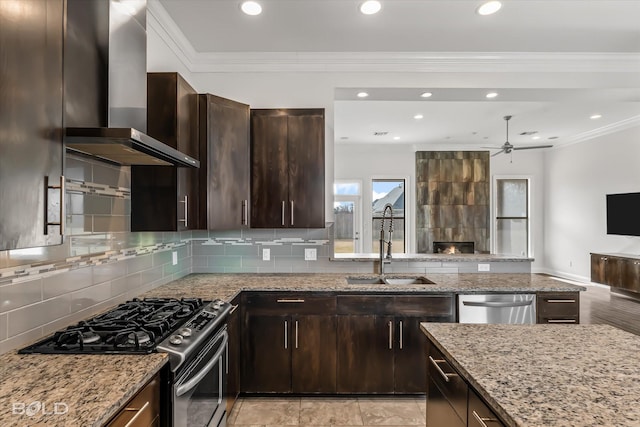 kitchen with wall chimney range hood, crown molding, sink, appliances with stainless steel finishes, and light stone counters