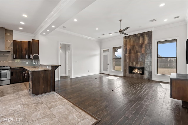 kitchen featuring a kitchen bar, dark brown cabinetry, a kitchen island with sink, sink, and stainless steel gas stove