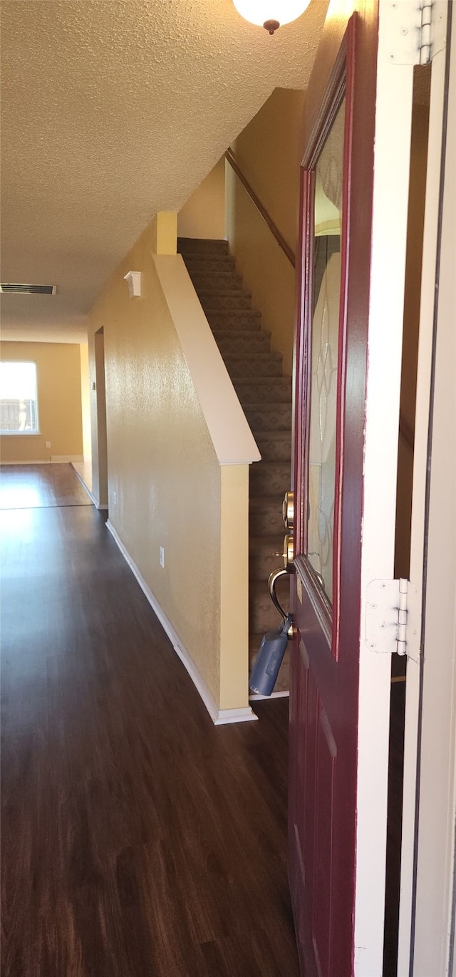 corridor with a textured ceiling, rustic walls, and dark wood-type flooring