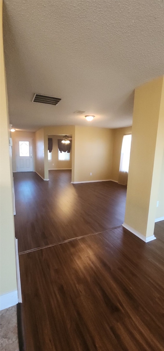 spare room with a textured ceiling, dark wood-type flooring, and a healthy amount of sunlight