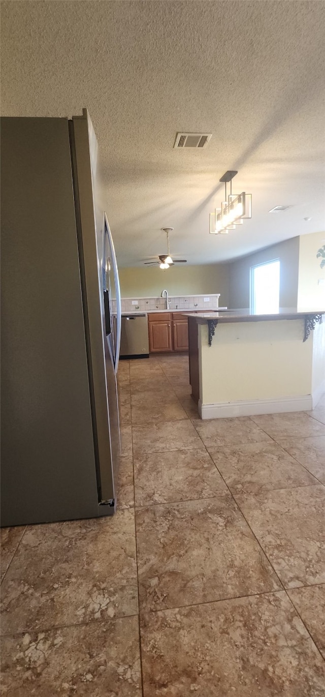 kitchen with a kitchen breakfast bar, sink, ceiling fan, a textured ceiling, and appliances with stainless steel finishes