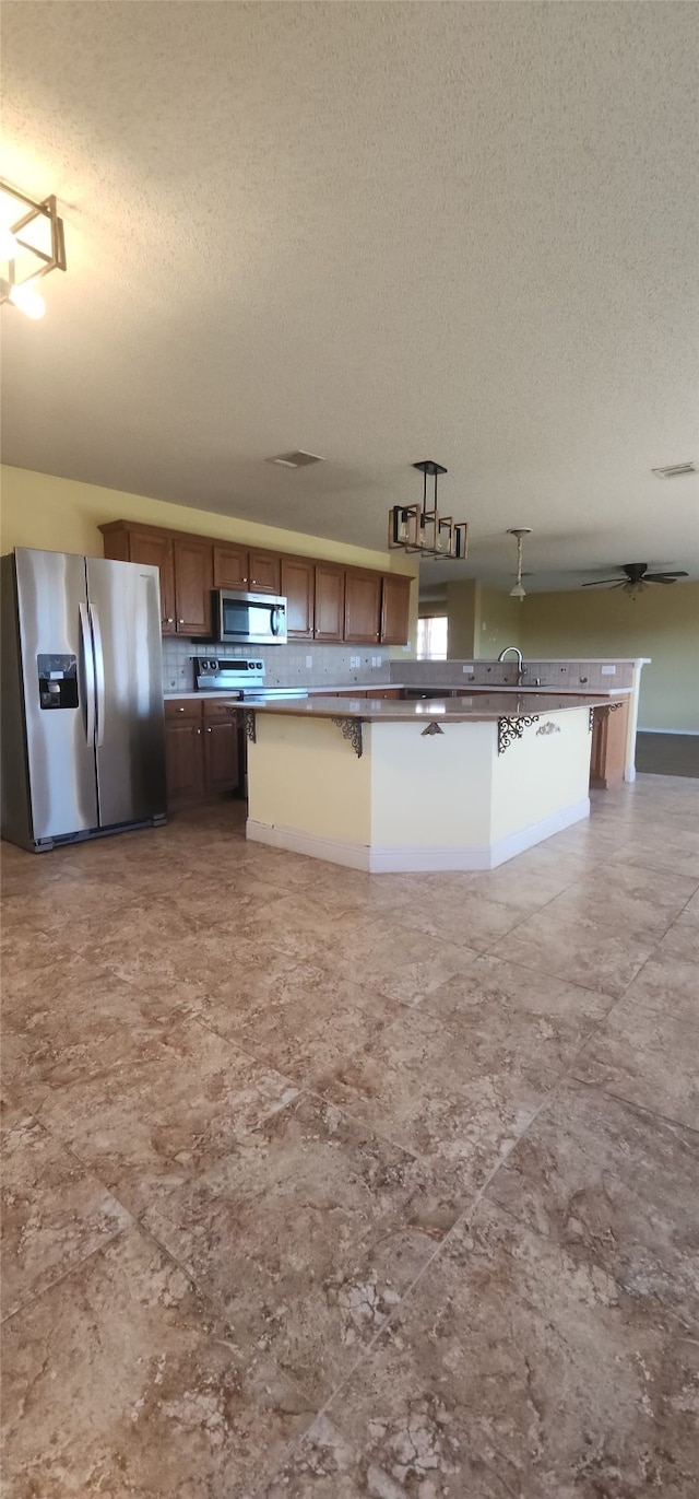 kitchen featuring a kitchen breakfast bar, hanging light fixtures, stainless steel appliances, and a textured ceiling