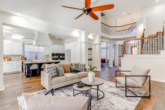 living room with ceiling fan, sink, light hardwood / wood-style floors, and a high ceiling