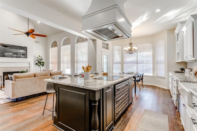 kitchen with a kitchen breakfast bar, custom exhaust hood, black electric cooktop, white cabinets, and an island with sink