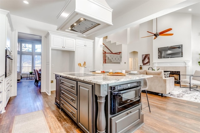 kitchen with light stone countertops, a center island, hardwood / wood-style floors, white cabinets, and black appliances