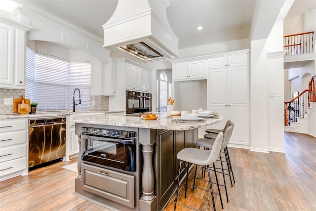 kitchen with backsplash, white cabinets, light hardwood / wood-style flooring, stainless steel dishwasher, and a kitchen island