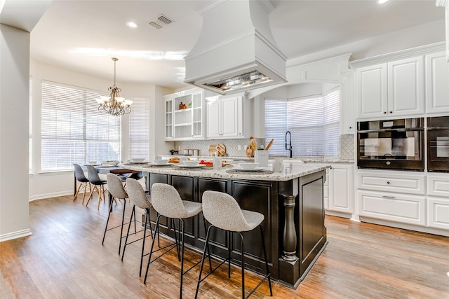 kitchen featuring light wood-type flooring, a kitchen island, pendant lighting, white cabinetry, and black oven