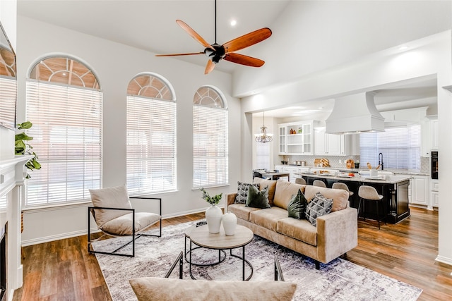 living room featuring wood-type flooring, ceiling fan with notable chandelier, lofted ceiling, and sink