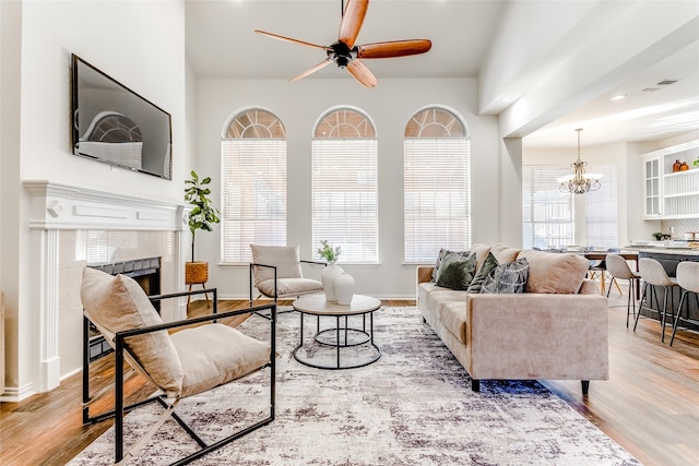 living room featuring a fireplace, light wood-type flooring, vaulted ceiling, and ceiling fan with notable chandelier