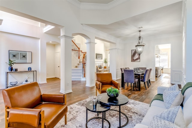 living room featuring decorative columns, light hardwood / wood-style flooring, ornamental molding, and an inviting chandelier