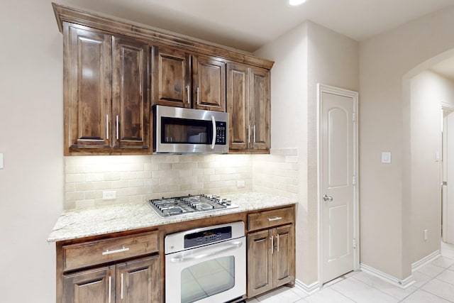 kitchen with decorative backsplash, stainless steel appliances, light stone countertops, and light tile patterned flooring