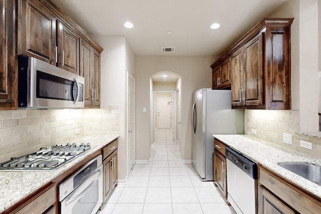 kitchen featuring backsplash, light stone countertops, light tile patterned flooring, and stainless steel appliances