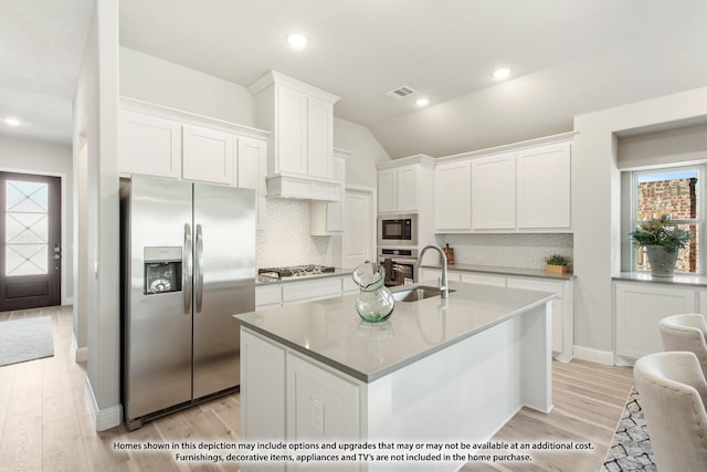 kitchen featuring light wood-type flooring, backsplash, stainless steel appliances, a kitchen island with sink, and white cabinets