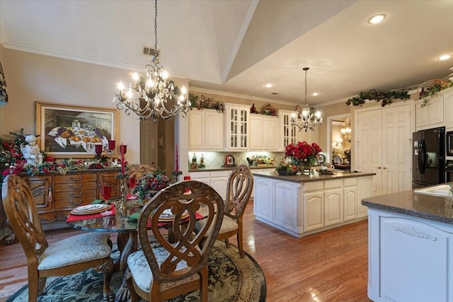 dining area featuring a chandelier, light wood-type flooring, vaulted ceiling, and crown molding