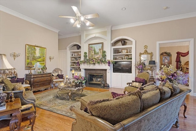 living room with hardwood / wood-style flooring, ceiling fan, built in features, and crown molding