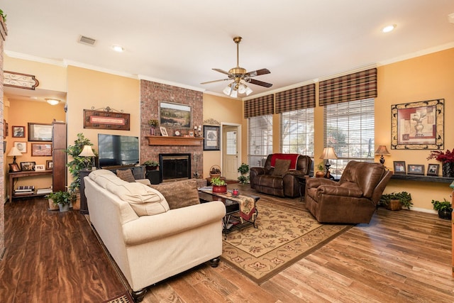 living room featuring a large fireplace, hardwood / wood-style flooring, ceiling fan, and ornamental molding