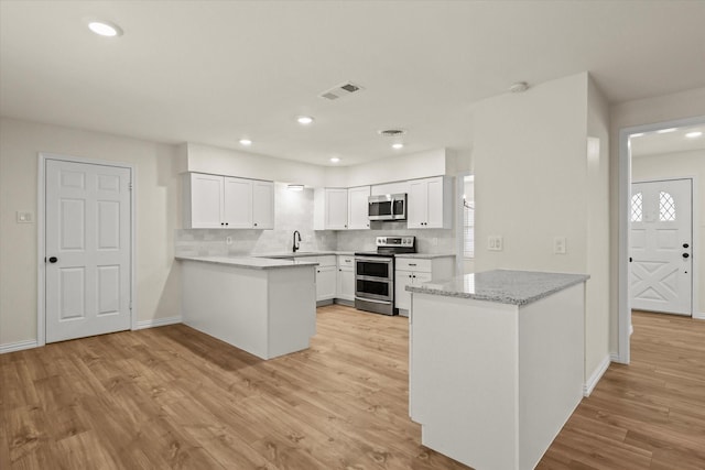 kitchen with kitchen peninsula, appliances with stainless steel finishes, white cabinets, and light hardwood / wood-style floors