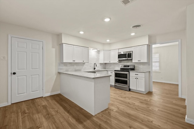 kitchen with kitchen peninsula, stainless steel appliances, white cabinetry, and light hardwood / wood-style floors