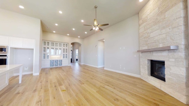 unfurnished living room featuring light hardwood / wood-style flooring, ceiling fan, and a stone fireplace