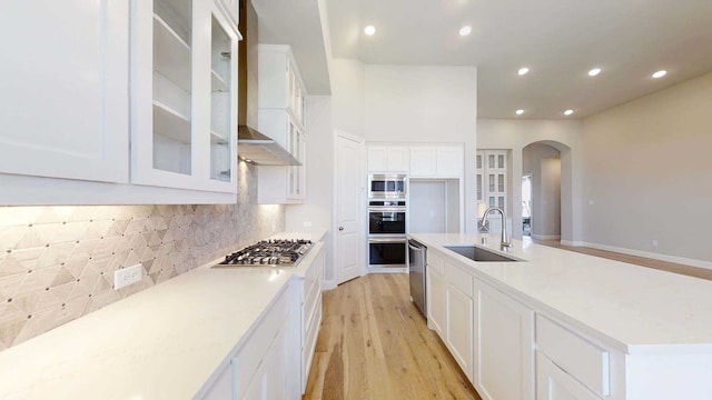 kitchen with white cabinetry, sink, wall chimney exhaust hood, stainless steel appliances, and light wood-type flooring