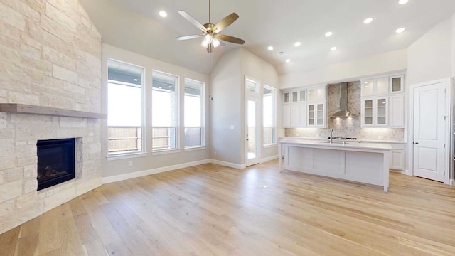 kitchen with white cabinetry, light wood-type flooring, wall chimney range hood, and an island with sink