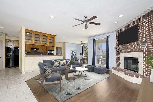 living room featuring ceiling fan, ornamental molding, light hardwood / wood-style floors, and a brick fireplace