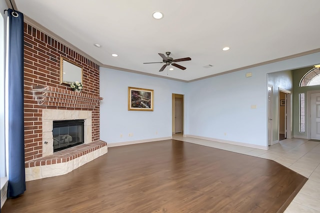 unfurnished living room with a brick fireplace, light tile patterned floors, ornamental molding, and ceiling fan