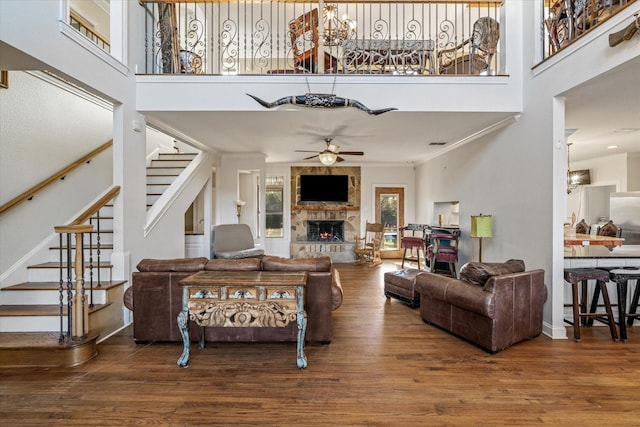 living room featuring ceiling fan, a stone fireplace, crown molding, a towering ceiling, and wood-type flooring