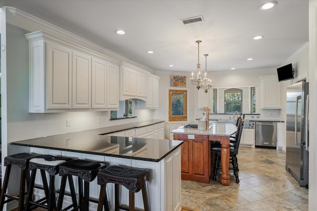 kitchen with kitchen peninsula, appliances with stainless steel finishes, white cabinetry, and a kitchen island