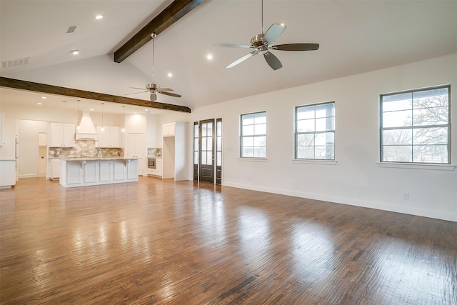 unfurnished living room featuring vaulted ceiling with beams, a wealth of natural light, and light hardwood / wood-style floors