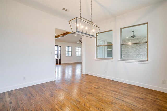 unfurnished dining area featuring hardwood / wood-style flooring, ceiling fan with notable chandelier, and beam ceiling