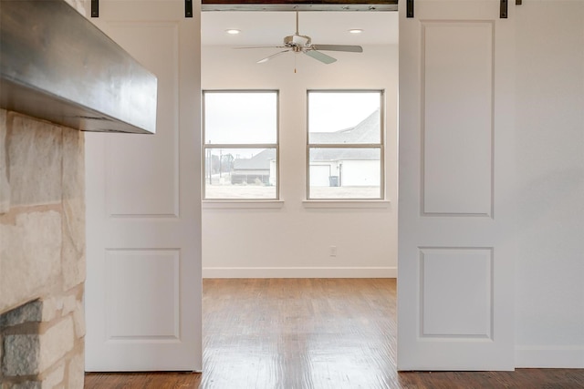 empty room featuring ceiling fan, a barn door, and wood-type flooring