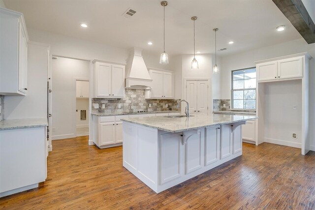 kitchen featuring white cabinets, hardwood / wood-style floors, premium range hood, and a kitchen island with sink