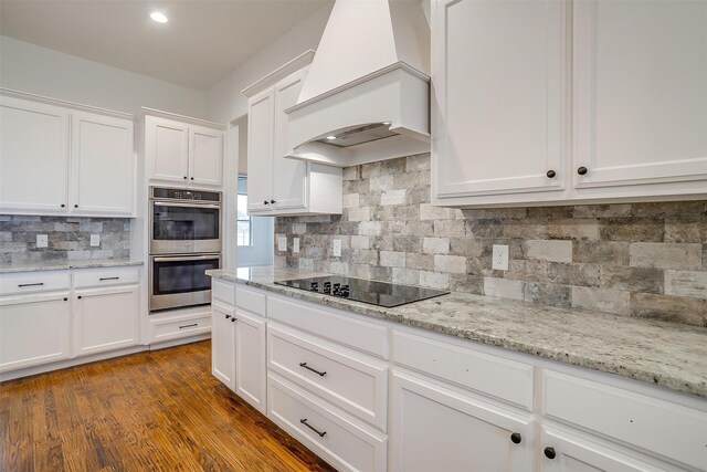 kitchen with black electric stovetop, backsplash, premium range hood, dark wood-type flooring, and white cabinetry