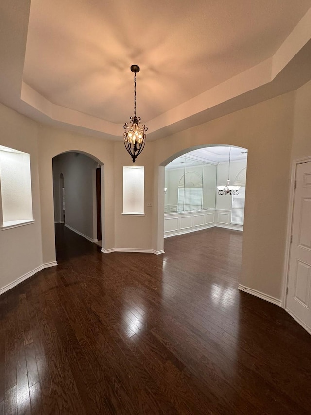 empty room featuring dark hardwood / wood-style floors, a tray ceiling, and an inviting chandelier