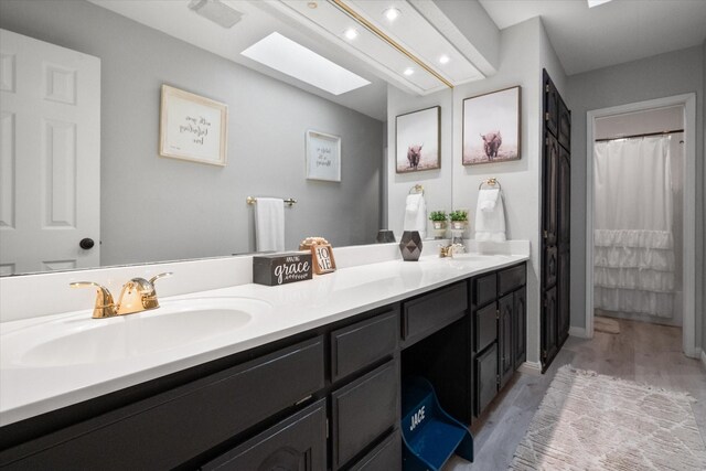 bathroom with hardwood / wood-style floors, vanity, walk in shower, and a skylight