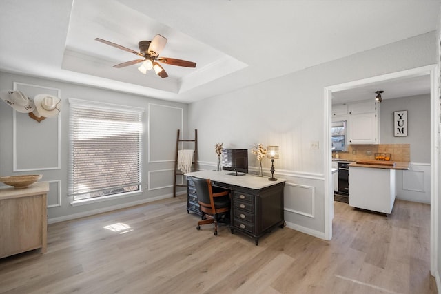 office space with a tray ceiling, light hardwood / wood-style flooring, and ceiling fan