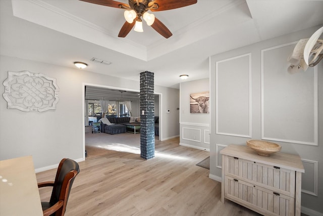 interior space with a raised ceiling, light hardwood / wood-style floors, ornate columns, and ornamental molding