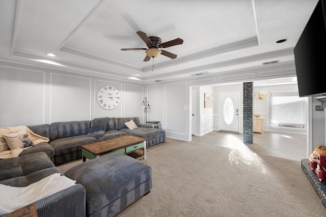 carpeted living room with a tray ceiling and ceiling fan