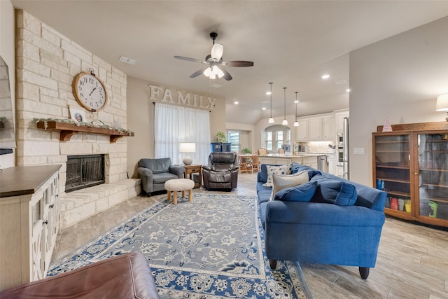 living room featuring ceiling fan, a stone fireplace, and light wood-type flooring