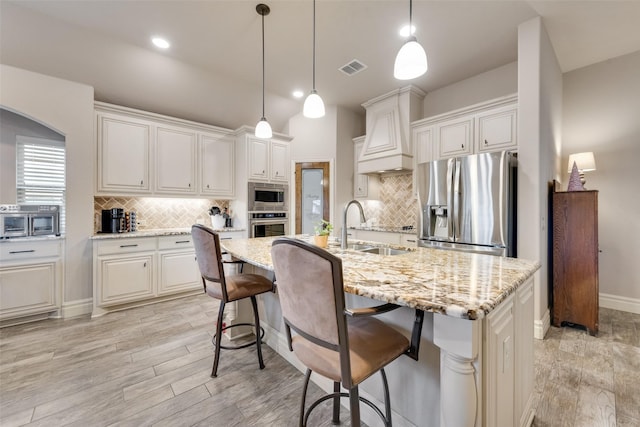 kitchen featuring white cabinetry, an island with sink, stainless steel appliances, and custom range hood