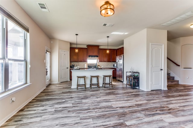 kitchen with a kitchen island with sink, a kitchen breakfast bar, hanging light fixtures, light hardwood / wood-style flooring, and stainless steel appliances