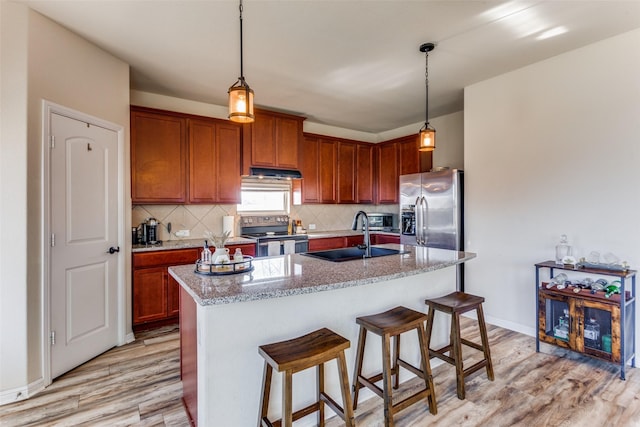 kitchen featuring light stone countertops, appliances with stainless steel finishes, sink, a center island with sink, and light hardwood / wood-style floors