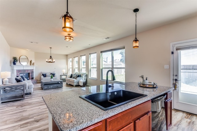 kitchen with pendant lighting, a center island with sink, sink, light wood-type flooring, and a fireplace