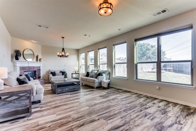 living room featuring a brick fireplace, a chandelier, and light wood-type flooring