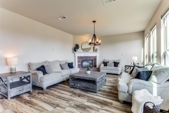 living room featuring wood-type flooring, an inviting chandelier, and a brick fireplace