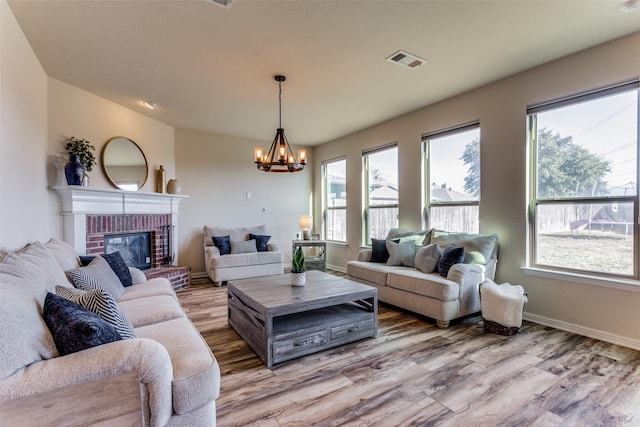 living room featuring a brick fireplace, light hardwood / wood-style flooring, and a notable chandelier